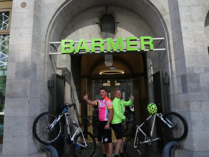 Zwei Barmer Mitarbeiter, die mit ihren Fahrräder ein V in der Eingangspforte von Barmer bilden